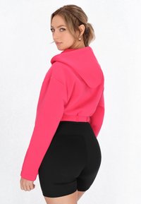 Klippt, huva sweatshirt i ljusrosa tyg med långa ärmar, matchad med högmidjade svarta shorts. Slät textur genom hela plagget.
