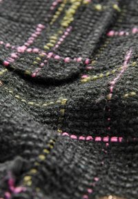 Tessuto nero a trama con un motivo scozzese arricchito da accenti rosa e gialli; cuciture evidenti creano profondità e dimensionalità.