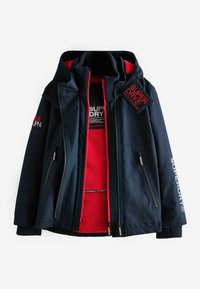Giacca esterna blu navy con interno in pile rosso, dotata di numerosi taschini con zip, polsini a coste e toppe con logo sul petto e sulla manica.