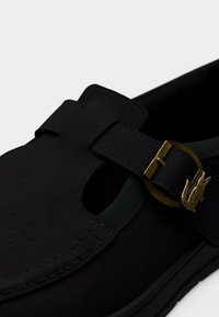 Μαύρο παπούτσι από λείο δέρμα με σχεδιασμό κοψίματος, διαθέτει πράσινη λεπτομέρεια και αγκράφα σε χρυσό τόνο με ανάγλυφο λογότυπο.