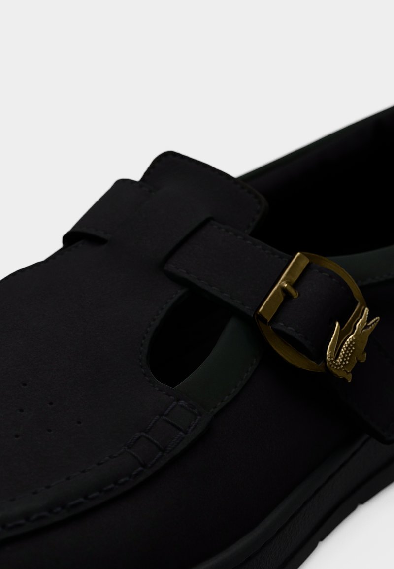 Scarpa nera in pelle liscia con design traforato, caratterizzata da un accento verde e una fibbia color oro con dettaglio logo in rilievo.