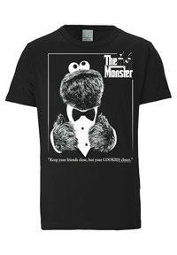 Camiseta de algodón negra con un personaje peludo en esmoquin, con el texto "El Monstruo" y una cita debajo en blanco.