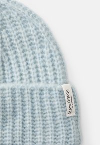 Căciulă tricotată de culoare albastră deschisă, cu o textură moale, având un tiv îndoit și un mic etichetă albă cu logo-ul "Marc O'Polo".