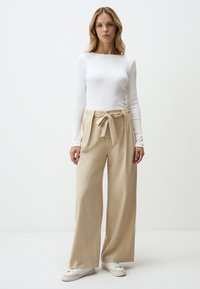 Beige wijde benen broek met een strik in de taille, gecombineerd met een aansluitend wit shirt met lange mouwen. Gladde textuur en minimalistisch ontwerp.
