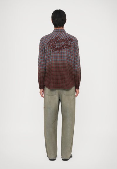 Geruite shirt met een verloopkleur van donkerrood naar blauw, voorzien van een groot geborduurd logo op de achterkant. Gecombineerd met losse, vervaagde groene broek.