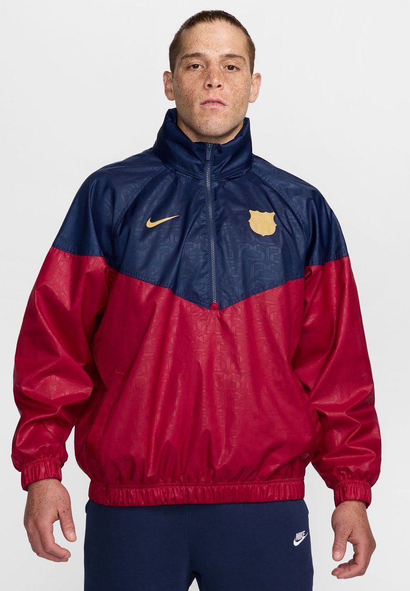 Kurtka przeciwwiatrowa Nike w niebieskiej górnej części i czerwonej dolnej, z fakturowanym wzorem, elastycznymi mankietami i złotym akcentem logo.