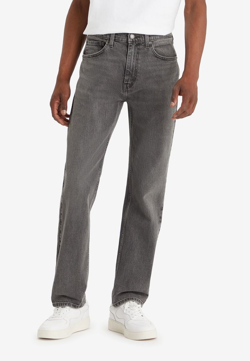 Jean en denim gris avec une coupe droite, cinq poches et fermeture frontale par boutons. Porté avec des baskets blanches.