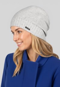 Grau gestrickte Mütze aus weichem Material mit geripptem Design und kleinem schwarzem Etikett. Passt eng an und hat eine lockere Form.