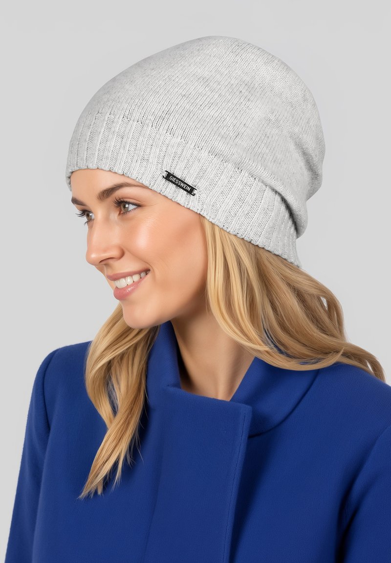 Grau gestrickte Mütze aus weichem Material mit geripptem Design und kleinem schwarzem Etikett. Passt eng an und hat eine lockere Form.