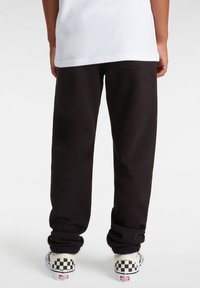 Zwarte sweatpants met een relaxte pasvorm en elastische boorden, gecombineerd met witte schoenen met een zwart-wit geblokt patroon.