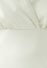 Gros plan d'un tissu blanc texturé avec un détail froncé et une couture en forme de V sur une section de vêtement.