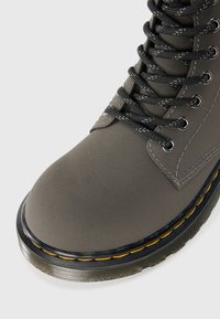 Bota cinza com atacadores, acabamento mate, bico redondo, ilhós reforçados e costura amarela em contraste ao longo da sola. Sola exterior em borracha durável.