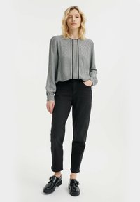Lichte grijze blouse met een gestructureerd ruitpatroon, voorzien van lange mouwen en een voorrits. Gecombineerd met zwarte jeans met hoge taille en stevige schoenen.