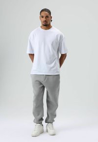 Witte korte mouw t-shirt en lichtgrijze sweatpants met elastische boorden. Witte sneakers met een gestructureerde zool, staand tegen een neutrale achtergrond.