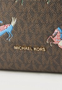 Καφέ υφασμάτινη τσάντα Michael Kors με χρυσλό λογότυπο και πολύχρωμες αφηρημένες απεικονίσεις α λόγων στην επιφάνεια.