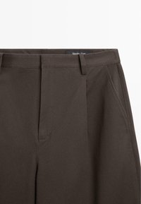 Dunkelbraune, maßgeschneiderte Hose mit Gürtelschlaufen, Seitentaschen und verdecktem vorderem Verschluss.