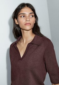 Bordeaux strikket top med V-hals og korte ærmer. Den bløde tekstur og det enkle design fremhæver stoffets subtile glans.