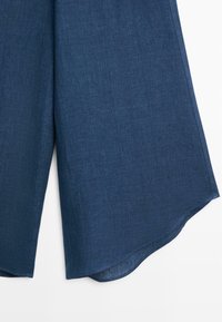 Pantalon bleu foncé à jambes larges en tissu texturé avec un ourlet légèrement incurvé sur fond blanc.