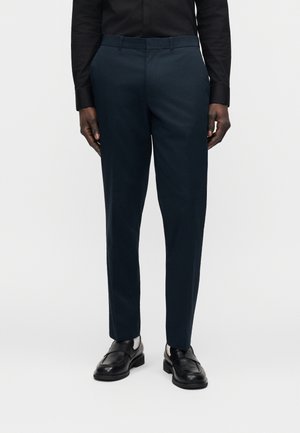 Marineblauwe, op maat gemaakte broek met een gladde textuur, een slank model en een standaard tailleband. Gecombineerd met zwarte leren schoenen.