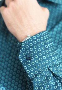 Close-up van een pols met een groenblauw geruit overhemd en een zilveren horloge gedeeltelijk zichtbaar onder de manchetten.