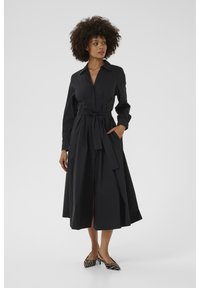 Black, long-sleeve shirt dress with a collar, tie waist, and side pockets, featuring a flowing skirt and a smooth texture. Zebra-print heels.