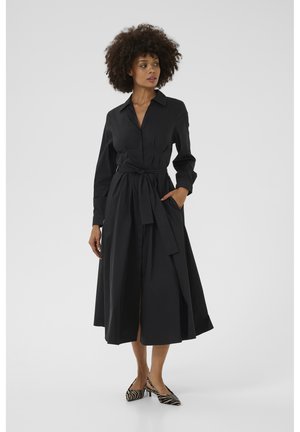 Black, long-sleeve shirt dress with a collar, tie waist, and side pockets, featuring a flowing skirt and a smooth texture. Zebra-print heels.