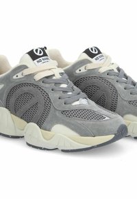 Zapatillas deportivas grises que combinan materiales de ante y malla, con una suela de goma prominente y acentos en crema contrastantes.