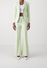 Completo su misura verde chiaro con un blazer aderente, due bottoni e pantaloni a zampa d'elefante. Indossato sopra un crop top bianco; abbinato a décolleté bianche a punta.