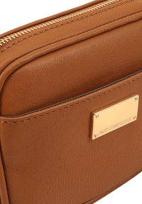 Sac bandoulière en cuir marron avec une finition texturée, doté d'une fermeture éclair dorée et d'une plaque nominative rectangulaire en métal.