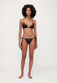 Črni bikini komplet s trikotnim zgornjim delom z prozornim robom in nastavljivimi naramnicami, v kombinaciji z boksericami na zavezovanje ob straneh, oba iz gladkega materiala.