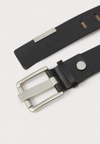 Ceinture en cuir noir avec boucle en métal argenté, portant le logo Calvin Klein. Texture lisse avec des trous réglables pour le dimensionnement.