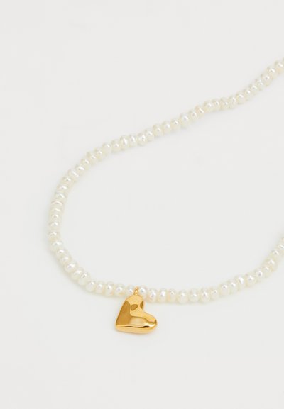 Colar de pérolas com um pequeno pingente em forma de coração dourado. O colar é composto por pérolas brancas redondas com uma textura lisa e brilhante. O encanto dourado tem a forma de um coração.
