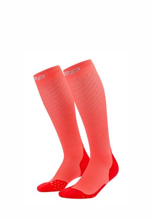 Pair of bright coral knee-high compression socks with subtle horizontal patterns and reinforced red toe and heel areas.