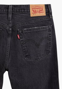 Jean en denim noir Levi's montrant la poche arrière droite avec l'étiquette rouge Levi's et un patch en cuir marron de la marque sur la ceinture.