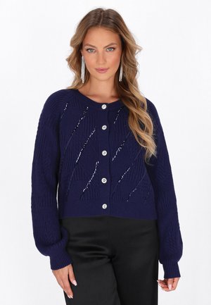 Tmavě modrý pletený cardigan s kulatým výstřihem, stříbrnými knoflíky na zapínání a dekoračním vzorem se slzičkami a vyvýšenými stehy.