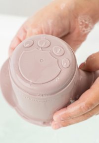 Roze siliconen beker met een glad oppervlak, voorzien van vier ronde knoppen bovenop, vastgehouden in een hand, met zichtbare waterdruppels.