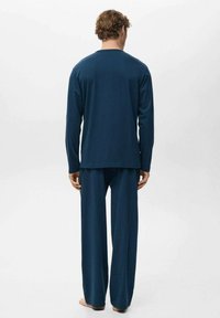 Conjunto de pijama azul marino hecho de tela suave. Top de manga larga con escote redondeado y pantalones holgados, ambos con una textura lisa.