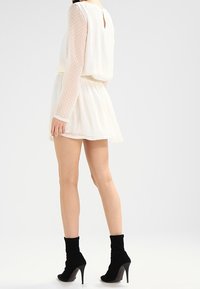Weißes Kleid mit langen, durchsichtigen gepunkteten Ärmeln und einem schwingenden Rock. Kombiniert mit schwarzen Knöchelstiefeln mit Stiletto-Absätzen.