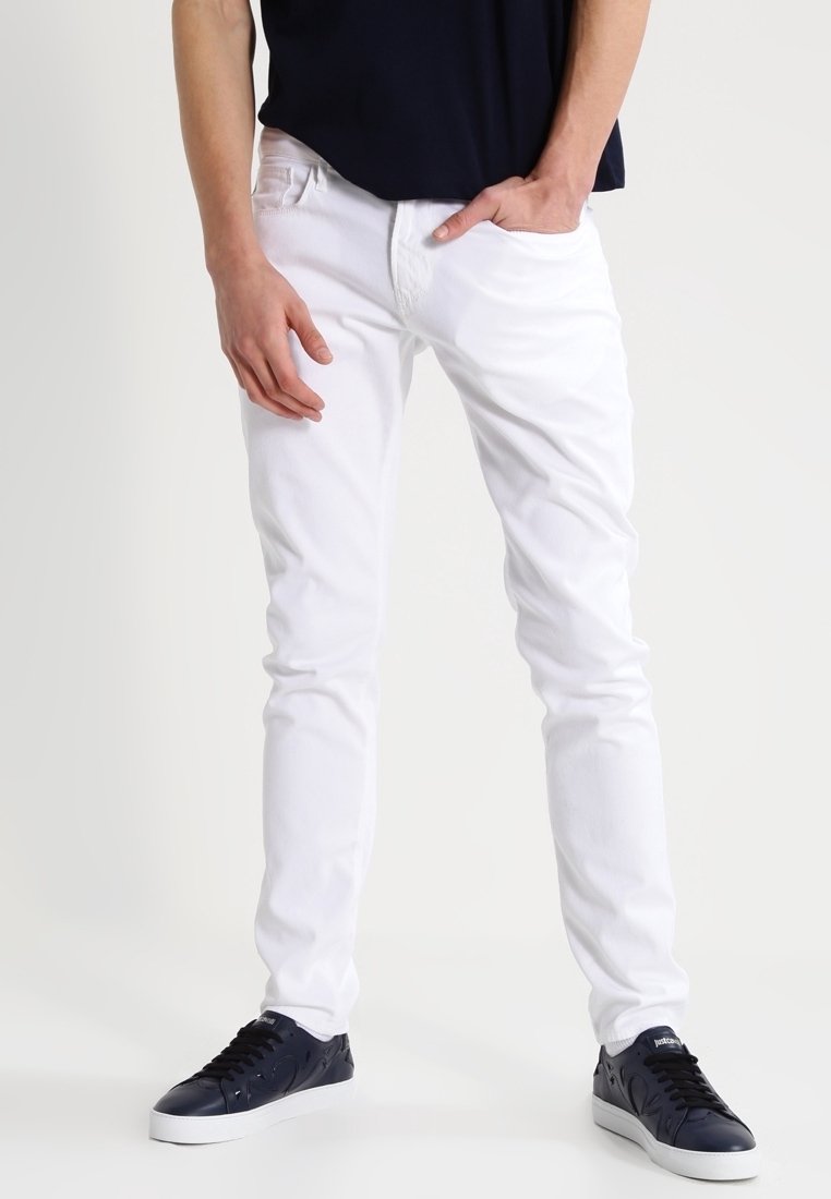 White denim jeans with a slim fit and five-pocket design, worn with navy sneakers. The fabric has a smooth texture and slight stretch.