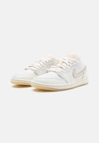 Biele kožené nízke tenisky s béžovým Nike swooshom, okrúhla špička, perforované detaily a textúrovaná gumová podrážka. Šnurovací dizajn.