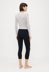 Maglia grigia chiaro a maniche lunghe con una sottile texture, abbinata a leggings neri a metà polpaccio con un elastico in vita e una forma aderente.