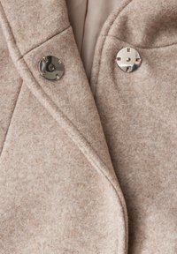 Manteau en laine beige avec une finition texturée, orné de boutons ronds en argent et d'un col châle, mettant en avant des lignes épurées et un design soigné.