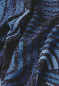 Strickstoff mit wellenförmigen Mustern in verschiedenen Blautönen und Schwarz. Weiche Textur mit einer Mischung aus dunklen und hellen Streifen.