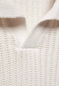 Suéter de punto en color crema, con cuello en V y un patrón texturizado. Tejido suave y ligero con un acabado acanalado. Detalles de diseño sutiles que realzan la apariencia.