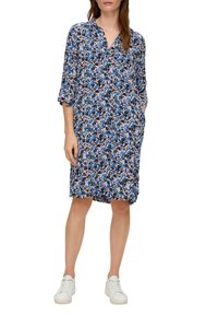 Kleid mit floralen Motiven in Blau, Pink und Weiß. Leichter Stoff, V-Ausschnitt, 3/4-Ärmel, Taschen, knielang, getragen mit weißen Turnschuhen.