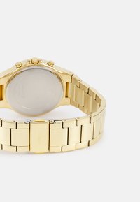 Montre en acier inoxydable doré avec un bracelet à maillons, dotée d'un boîtier rond, de trois boutons chronographes et d'un dos en métal lisse.