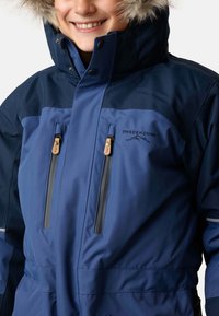 Blå vattentät jacka med pälsfodrad huva, fickor med dragkedja och logodetaljer. Den har en slät struktur och justerbar passform.