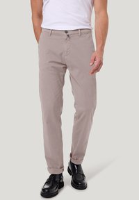 Beige katoenen broek met een rechte pasvorm, voorzien van een knoopsluiting en opgerolde manchetten, gecombineerd met zwarte leren schoenen.