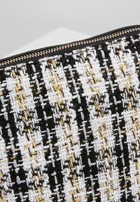 Gros plan sur un tissu tissé noir, blanc et or avec une fermeture éclair métallique le long du bord.