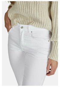 Witte denim jeans met een slim fit, voorzien van een voorkantzak, knoopsluiting en subtiele stikdetails, gecombineerd met een beige gebreide trui.